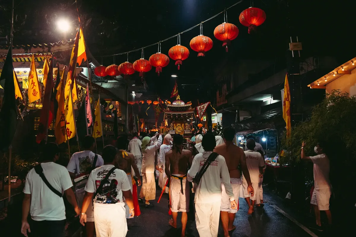 Colorful night parade during the Phuket Vegetarian Festival with participants in traditional attire and glowing lanterns.